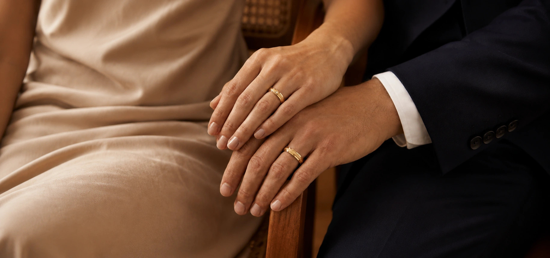 Mãos de casal sobrepostas, com alianças Nuance em ouro 18k
